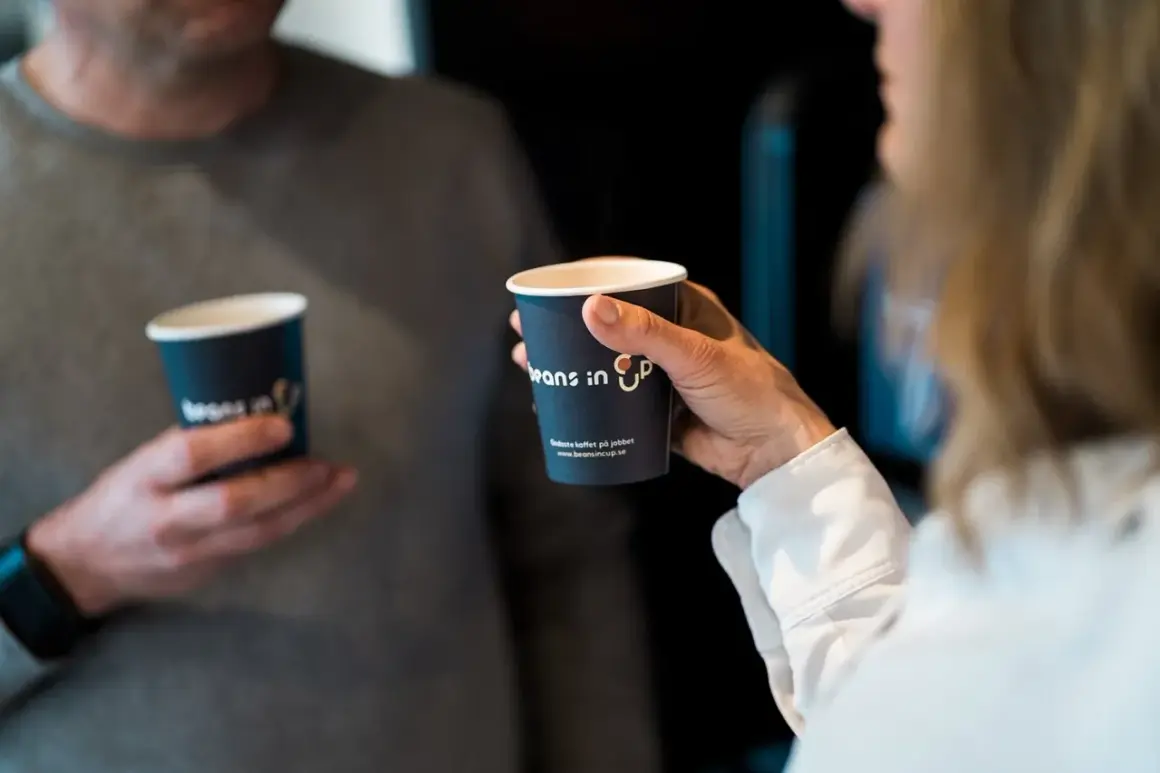 Två personer håller kaffemuggar. En kvinna håller en mugg med texten "Beans in Up". Kanske är det här svaret på vilket land dricker mest kaffe.