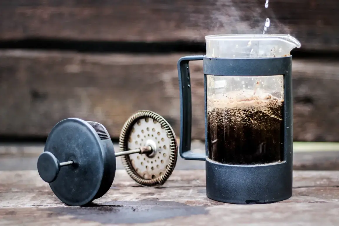 Varmt vatten hälls över kaffepulver i en presskaffe i kaffebryggare. Ånga stiger från den nybryggda drycken.
