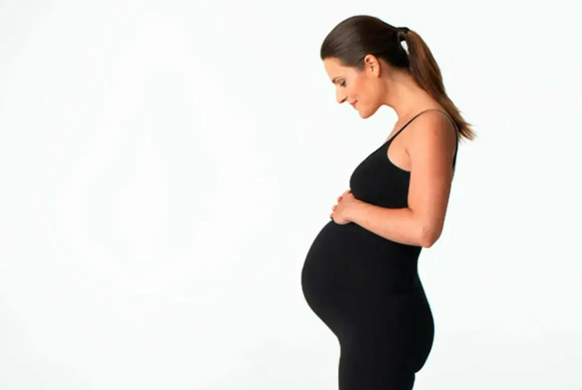 Gravid kvinna i svart klänning håller om sin mage. Hon ser lycklig ut, kanske hon funderar på att ta ginseng för energi.