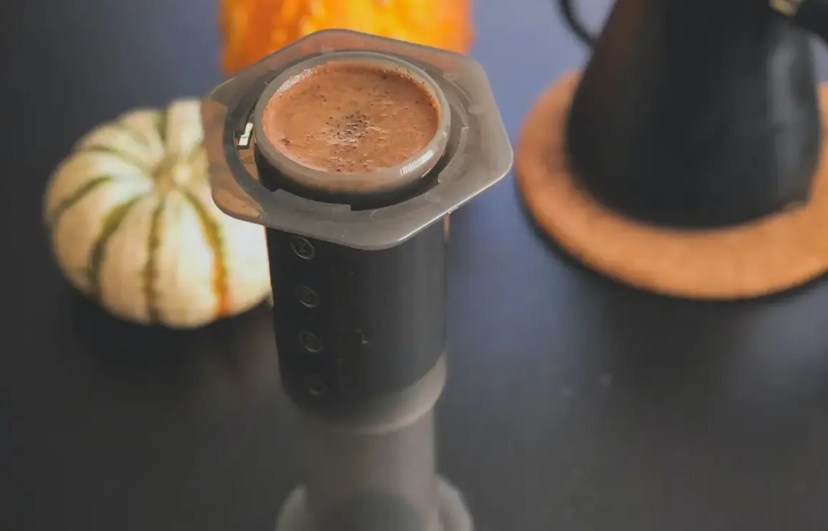 En kopp aeropress kaffe med en pumpa i bakgrunden.