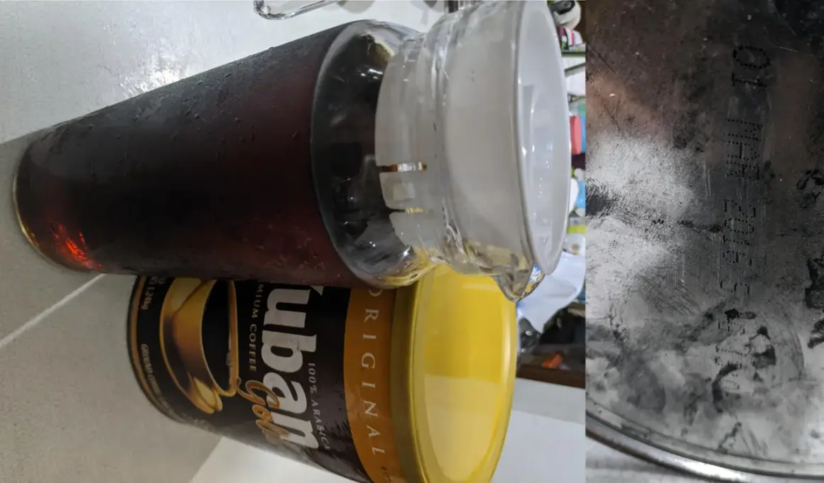 En stor glasburk med kondens fylld med mörkt, gammalt kaffe står bredvid en gul burk med "ubán Gold" kaffe.
