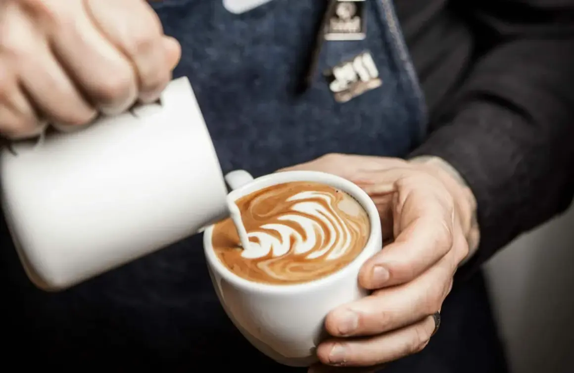 Barista skapar vacker latte art genom att hälla mjölk i en kaffekopp.