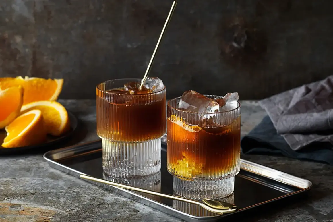 Två glas med kaffe tonic, is och apelsinskivor på ett fat.