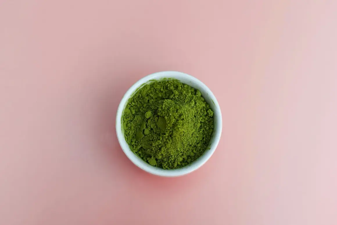 En skål med intensivt grönt matchapulver på en mjukrosa bakgrund. Undrar du vad smakar matcha? Det är en unik, lite bitter och gräsig smak.