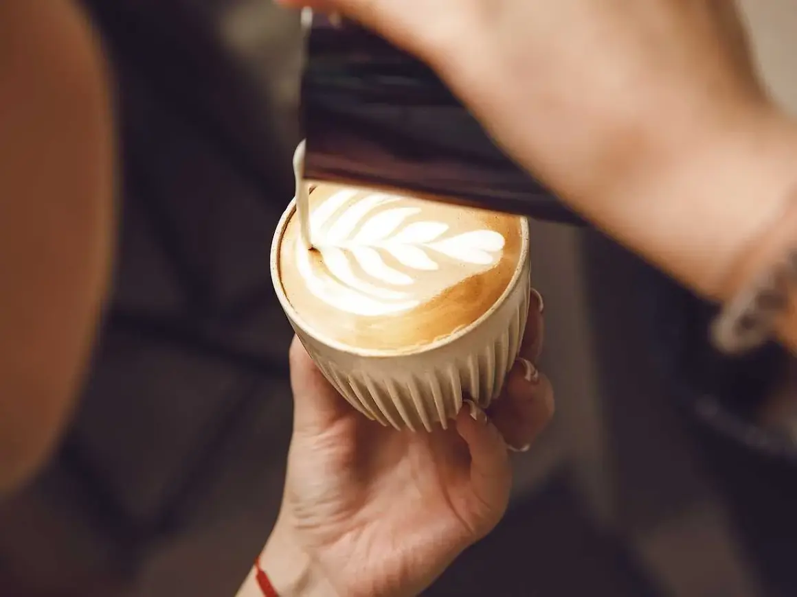 En barista skapar vackert latte art i en kopp kaffe latte.