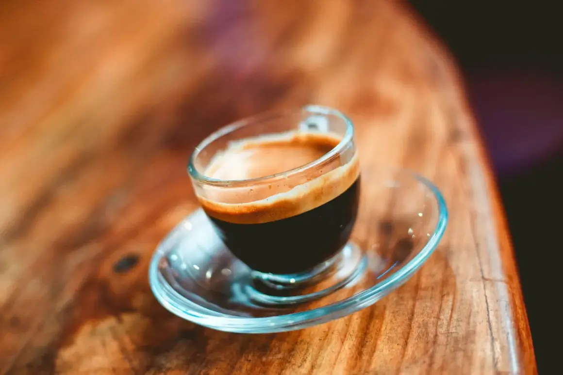 En kopp med en gyllene crema, en perfekt lungo kaffe, står på ett träbord.