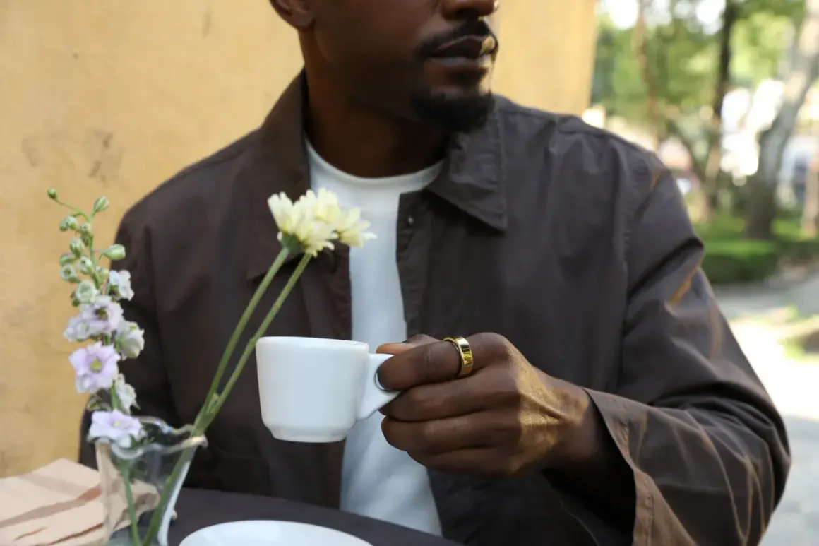Man med guldig ring håller en vit kopp med te. Koffein ger energi för dagen.