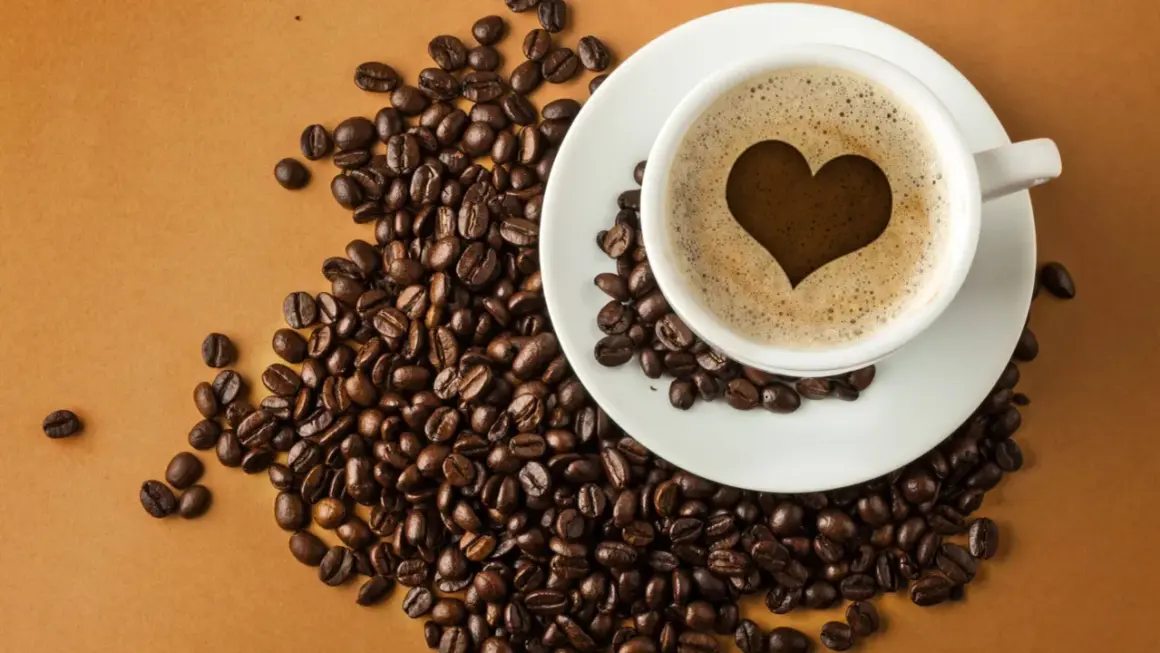 En kopp kaffe med ett hjärta i skummet, omgiven av kaffebönor. En visuell förklaring till hur fungerar koffein.