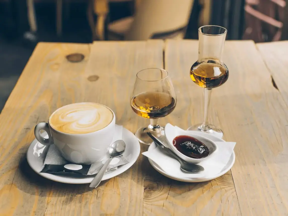 En kopp kaffe med vitt hjärta på skummet, bredvid två glas med bärnstensfärgad dryck och en skål med sylt. En perfekt kombination för en stunds njutning.