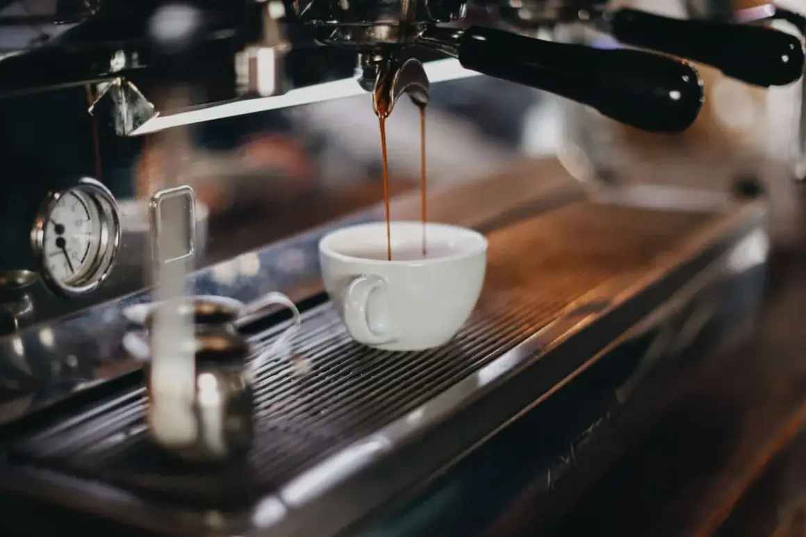 Espresso rinner ner i en vit kopp. En liten mjölkkanna står bredvid, redo för att skapa perfekt kaffeskum.