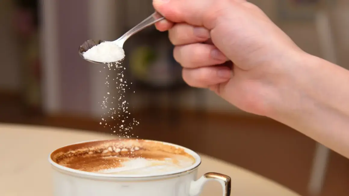 En hand häller socker från en sked ner i en kopp kaffe. Kanske är det salt i kaffet istället för socker?