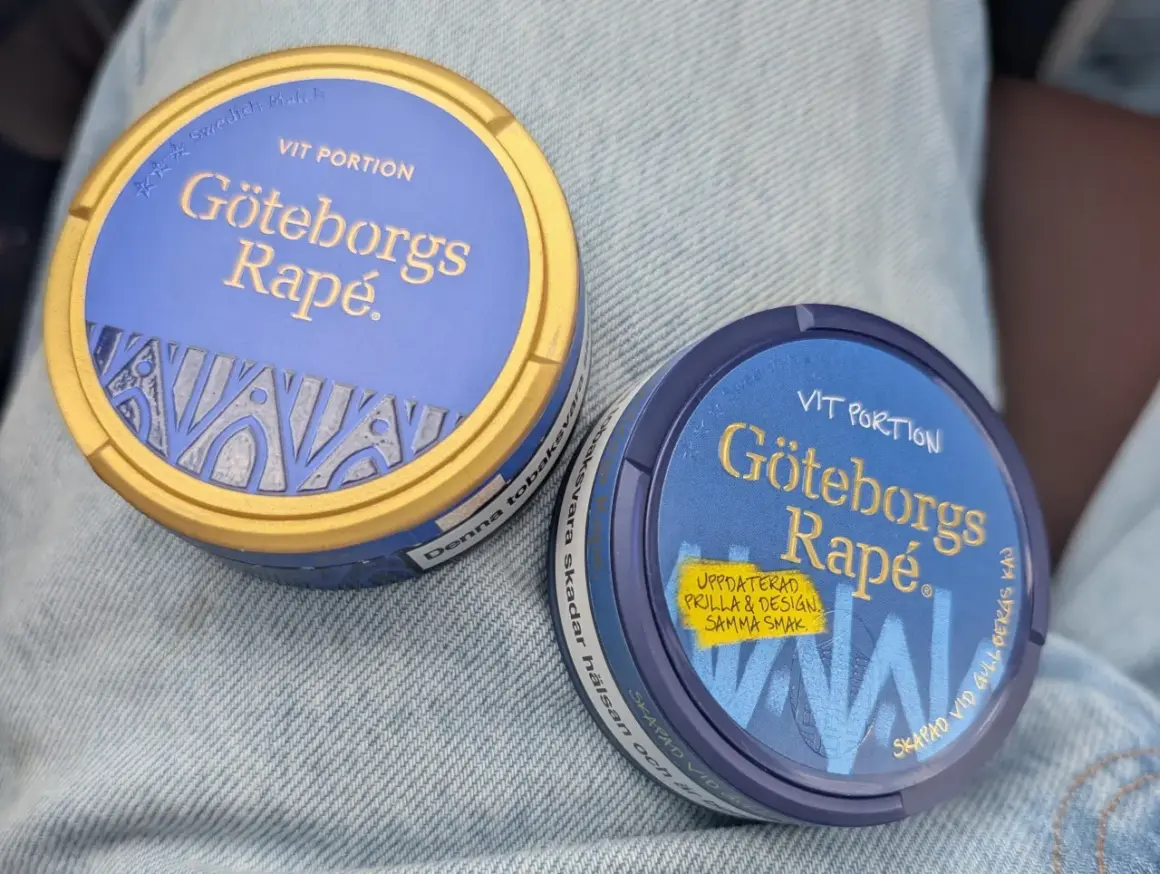Två dosor Göteborgs Rapé, en med guldig kant, ligger på jeans. Perfekt för dig som vill ha snus som inte rinner.