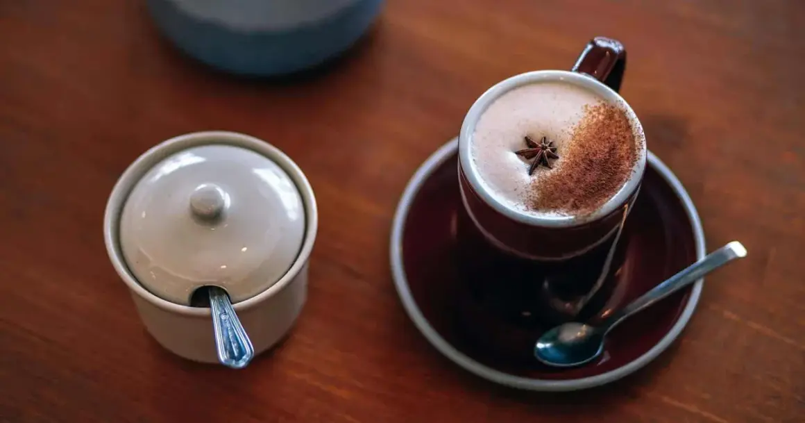 En kopp värmande chai latte med stjärnanis och kanel, bredvid en sockerskål med sked.