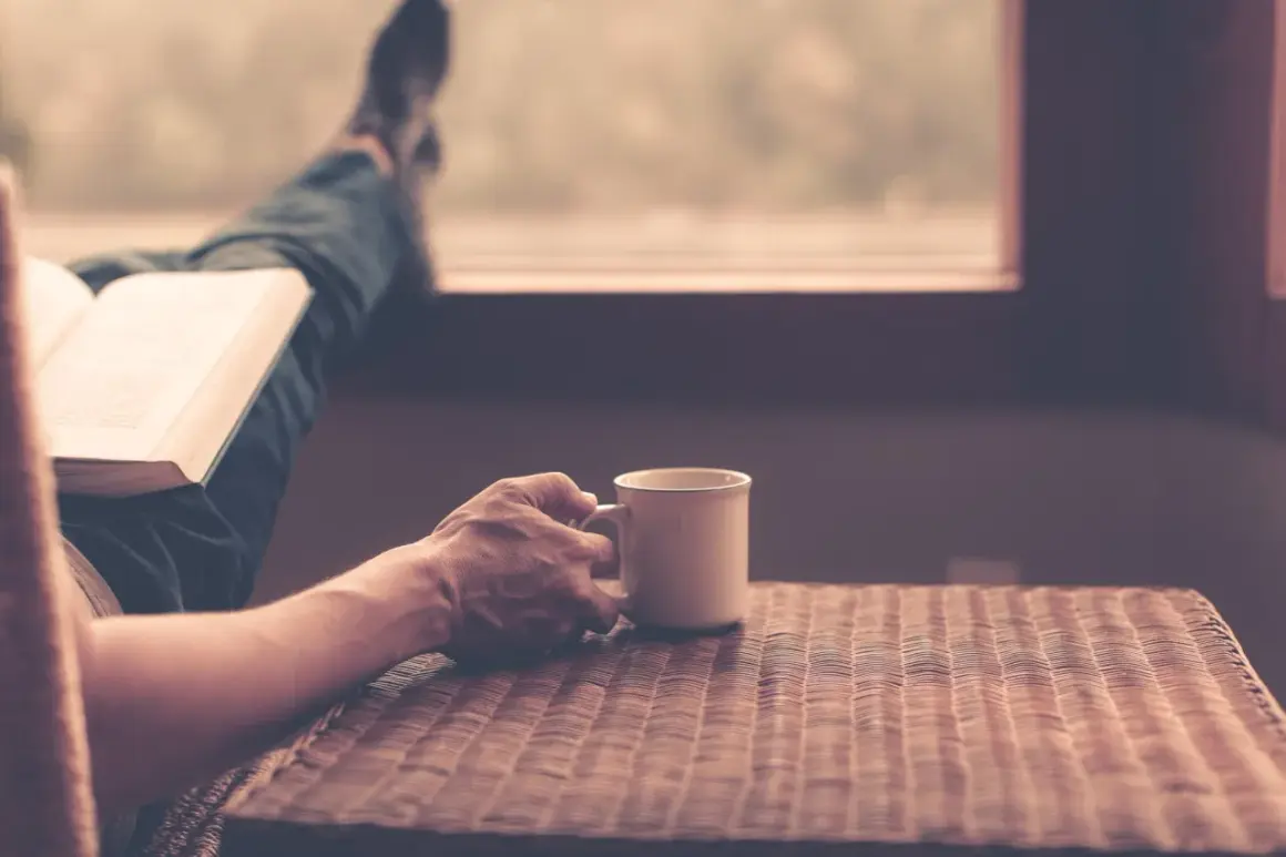 En person läser en bok med en kopp kaffe, njuter av stunden och funderar över kaffe ursprung.