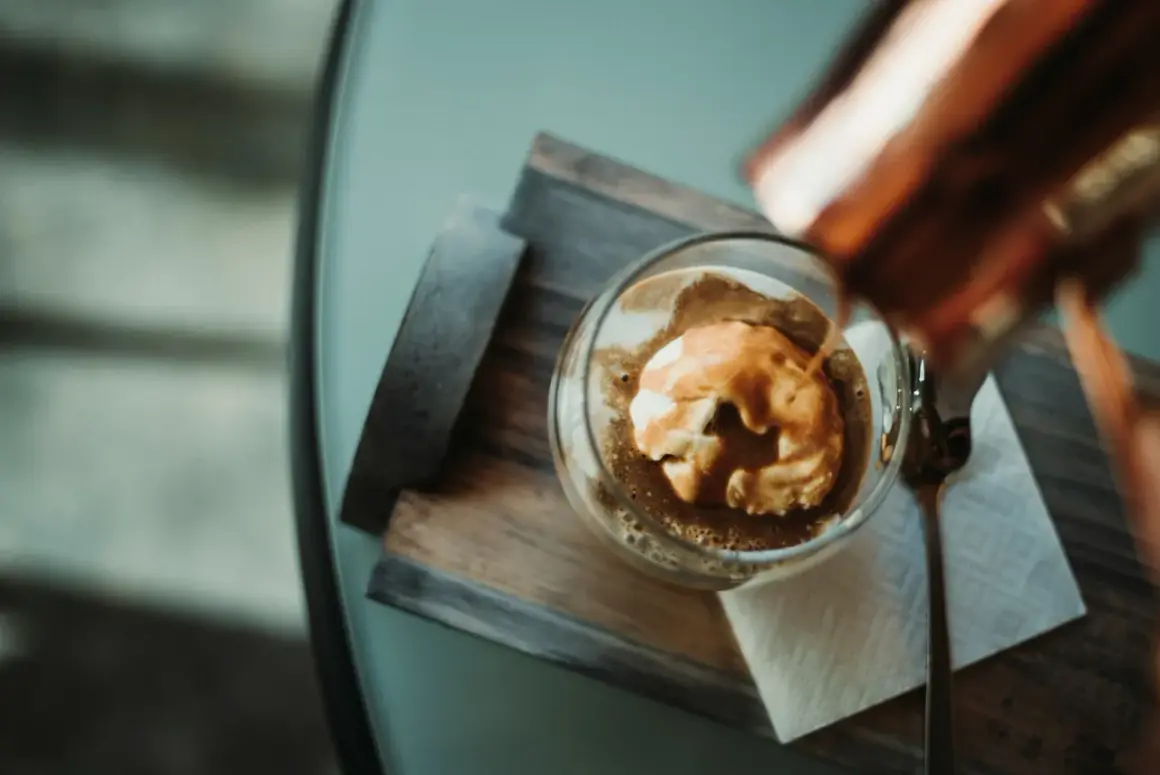 Varm espresso hälls över vaniljglass i en klassisk cafe affogato. En sked ligger bredvid.