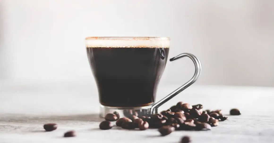 En kopp mörkt kaffe med skum och kaffebönor. Vitt te nyttigt, men en kopp kaffe ger också energi.