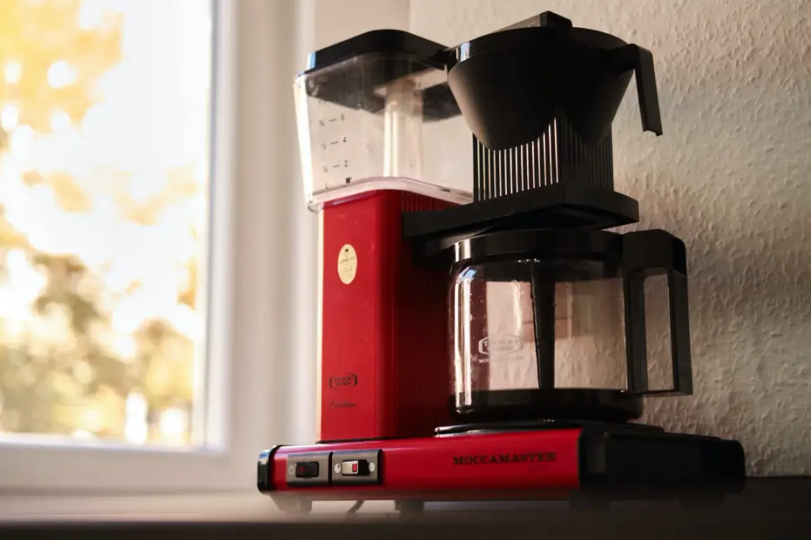 Röd Moccamaster kaffebryggare vid fönstret, redo att brygga en god kopp kaffe.