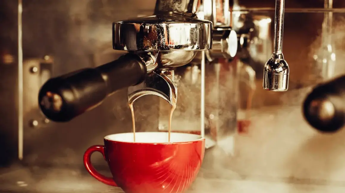 En röd kopp fylls med rykande espresso från en maskin. En klassisk italiensk kaffeupplevelse.