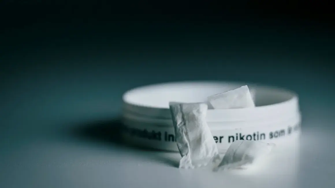 En dosa snus, ett populärt naswar i Sverige, med några påsar framför.
