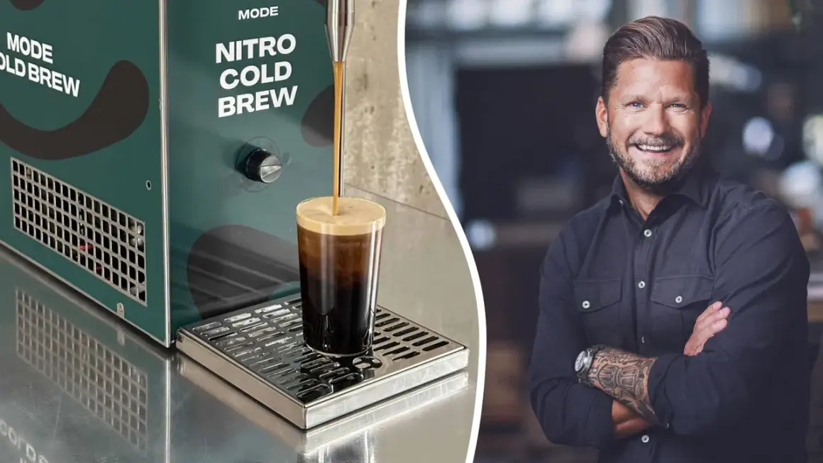 En leende man med tatueringar på armen bredvid en maskin som gör nitro cold brew.