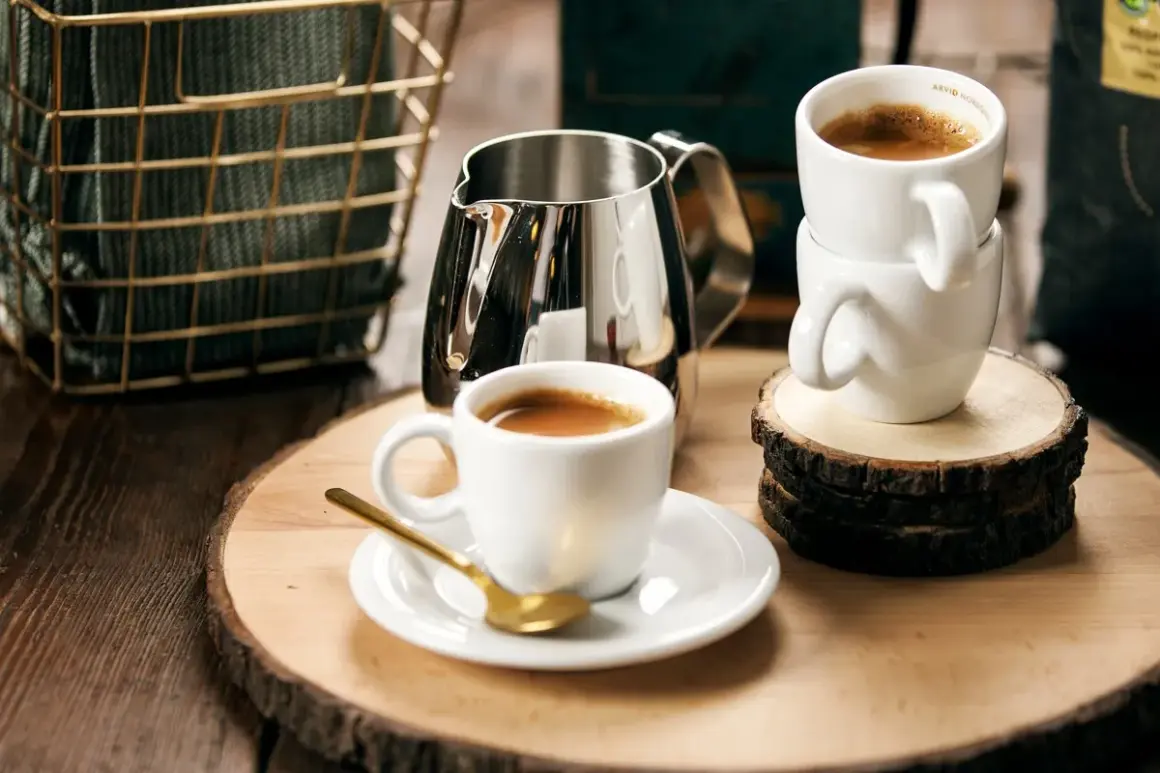 Enkel espresso i vit kopp med guldfärgad sked. En mjölkkanna och en stapel koppar står bredvid.