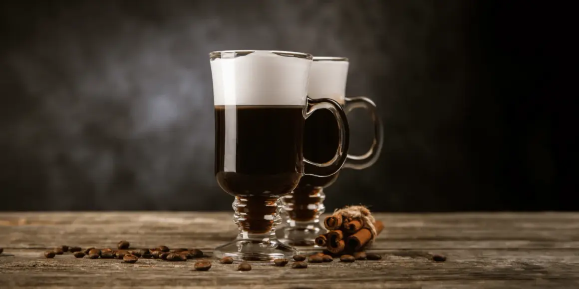 Två glas med krämig cappuccino, kaffebönor och kanelstänger. Perfekt för ett mysigt cappuccino recept.