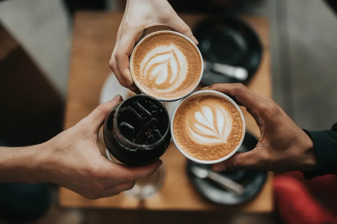 Tre händer håller varsin kopp med kaffe. Två koppar har vacker latte art, en är en kaffe macchiato.