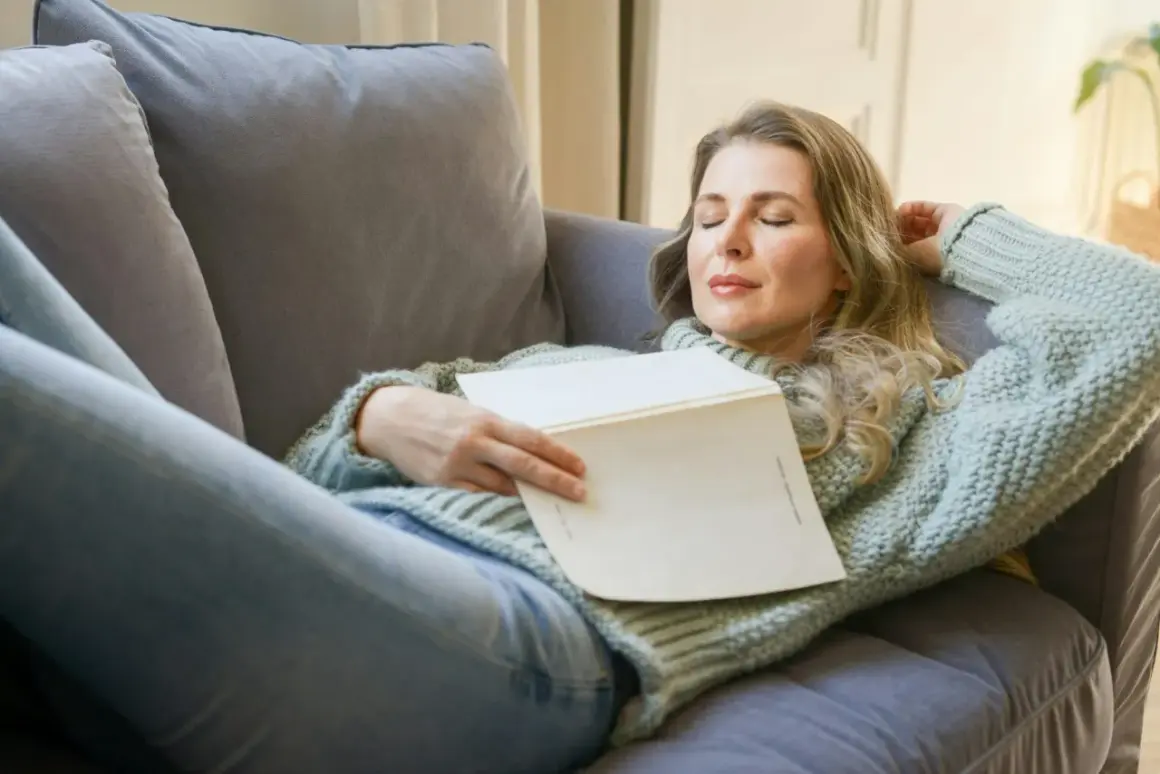 Kvinna vilar på soffan med en bok i famnen, drömmer om hur lång ska en powernap vara för maximal återhämtning.