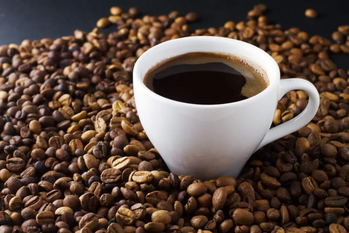 En vit kopp med mörkt, ångande kaffe omgiven av grovmalet kaffe. En perfekt start på dagen.