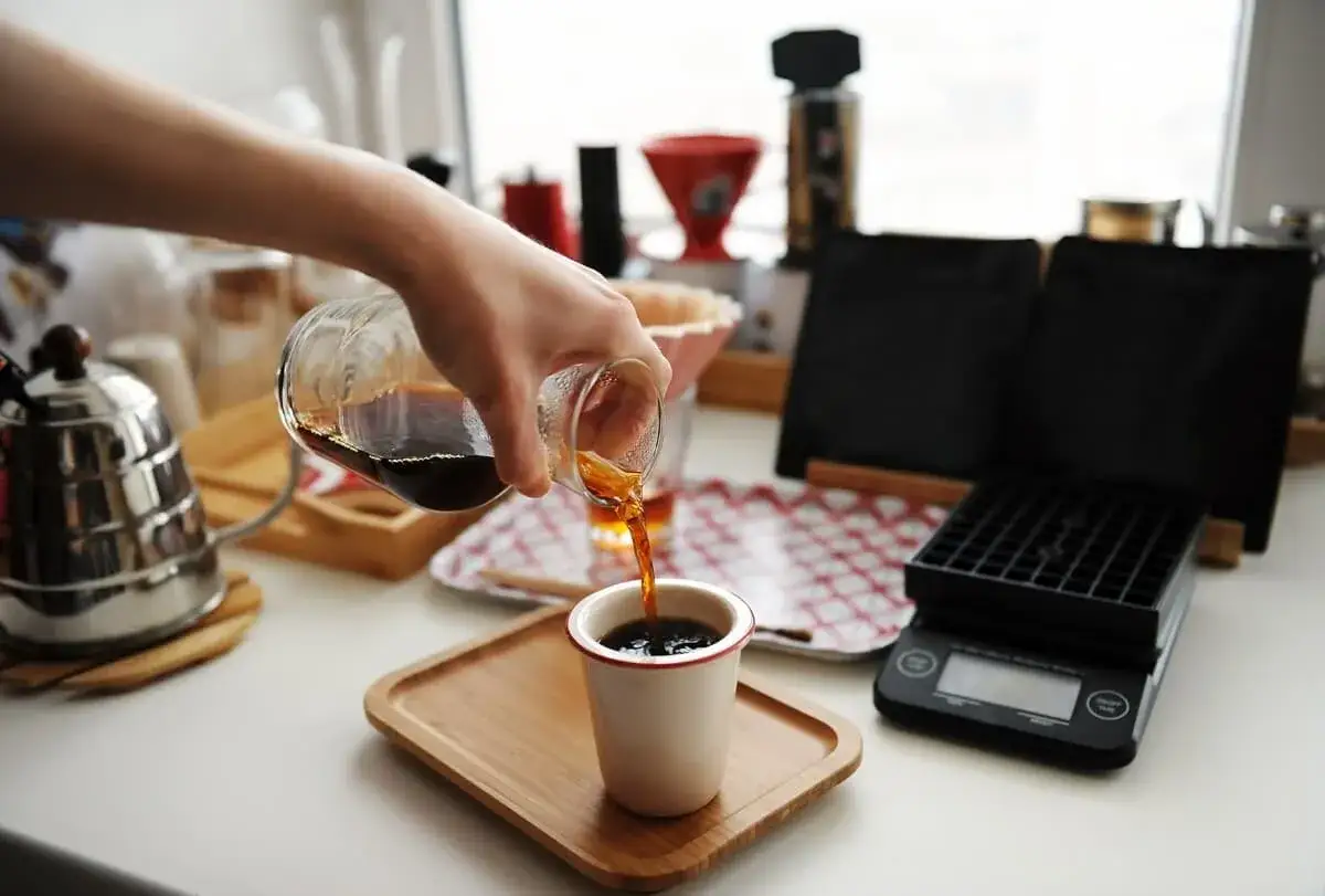 En hand häller upp nybryggt kaffe i en mugg. En vacker demonstration av hur brygger man kaffe med precision och omsorg.