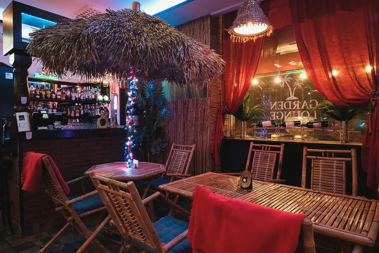 Mysigt vattenpipa cafe med bambumöbler, röda draperier och tropisk inredning. Perfekt för en avslappnad kväll.