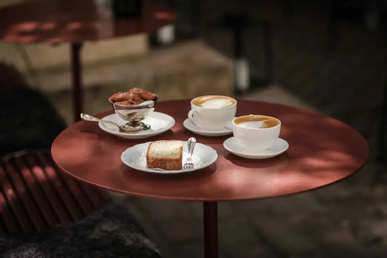 Två kaffekoppar med latte art, en bit kaka och chokladmousse på ett bord. En perfekt fika för att välja mellan latte macchiato vs cappuccino.