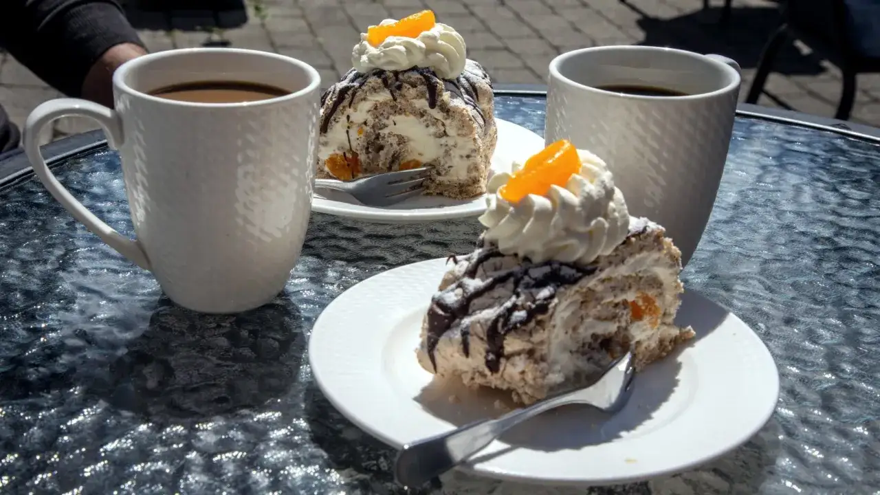 Två koppar med vitt kaffe och två bitar av en rulltårta med grädde och apelsin på ett glasbord.
