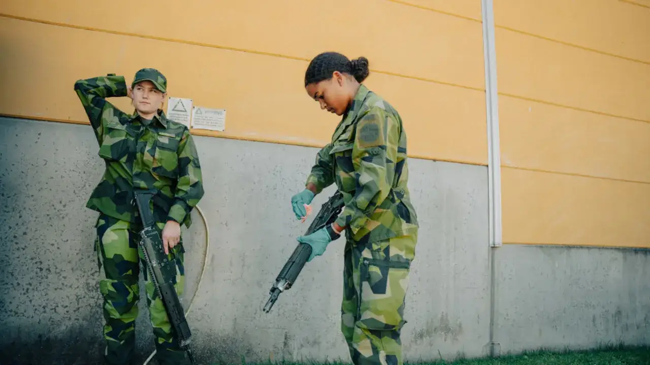 Två soldater i lumpen, en med handen bakom huvudet, den andra putsar ett vapen.
