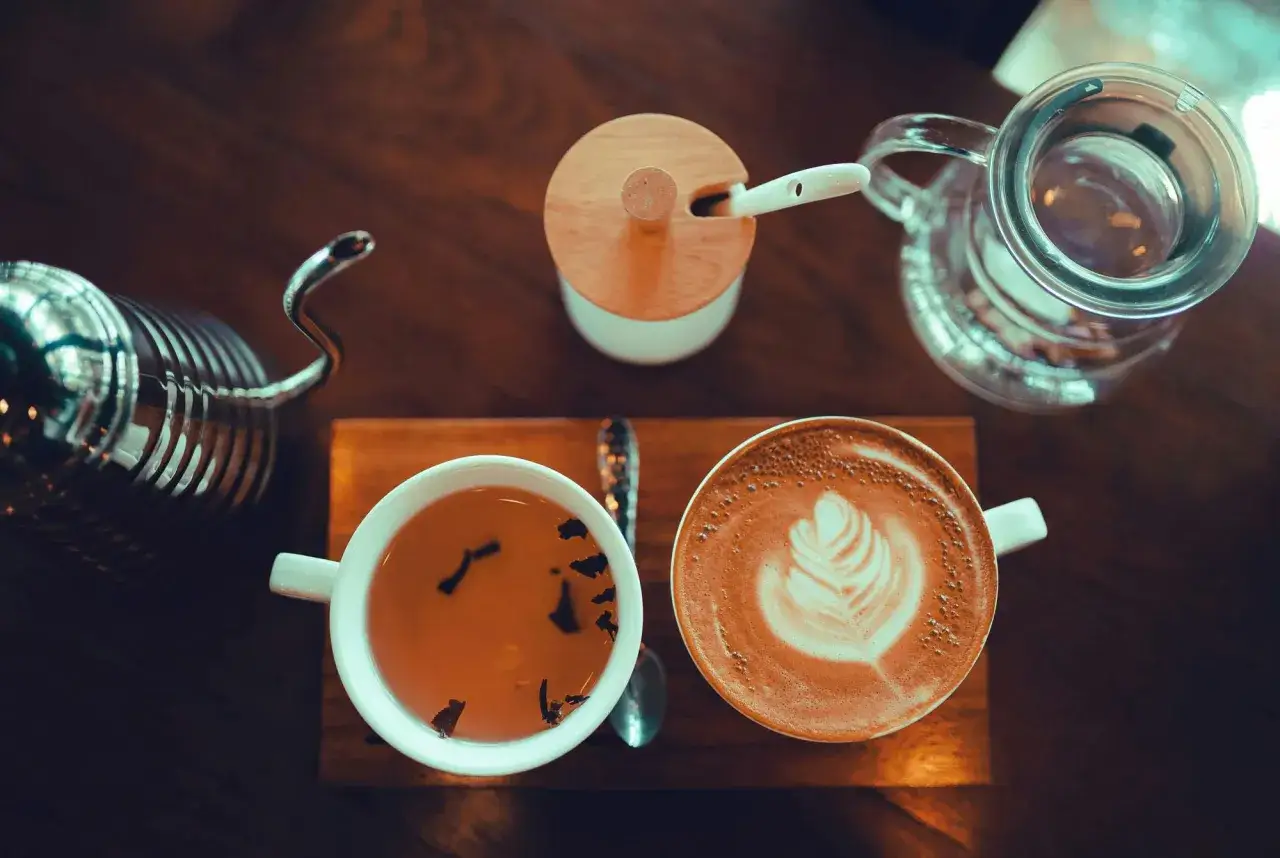 En kopp te och en latte p&aring; ett tr&auml;bord. En tekanna och en sockersk&aring;l syns ocks&aring;. Hur m&aring;nga koppar te per dag &auml;r en bra fr&aring;ga att st&auml;lla sig.