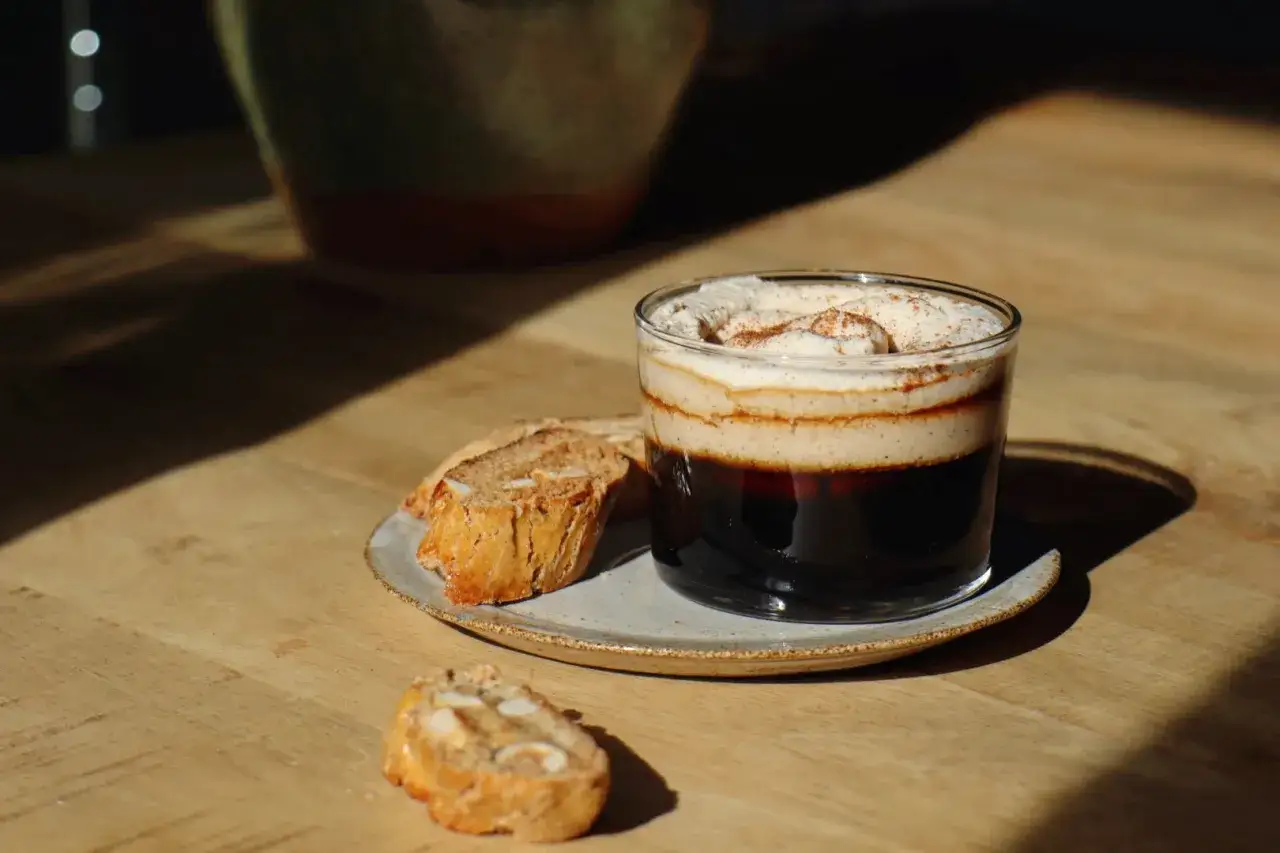 Kaffe med fluffigt skum och kanel, serverat med mandelkakor. Perfekt för en stunds avkoppling med rätt rostas temperatur.