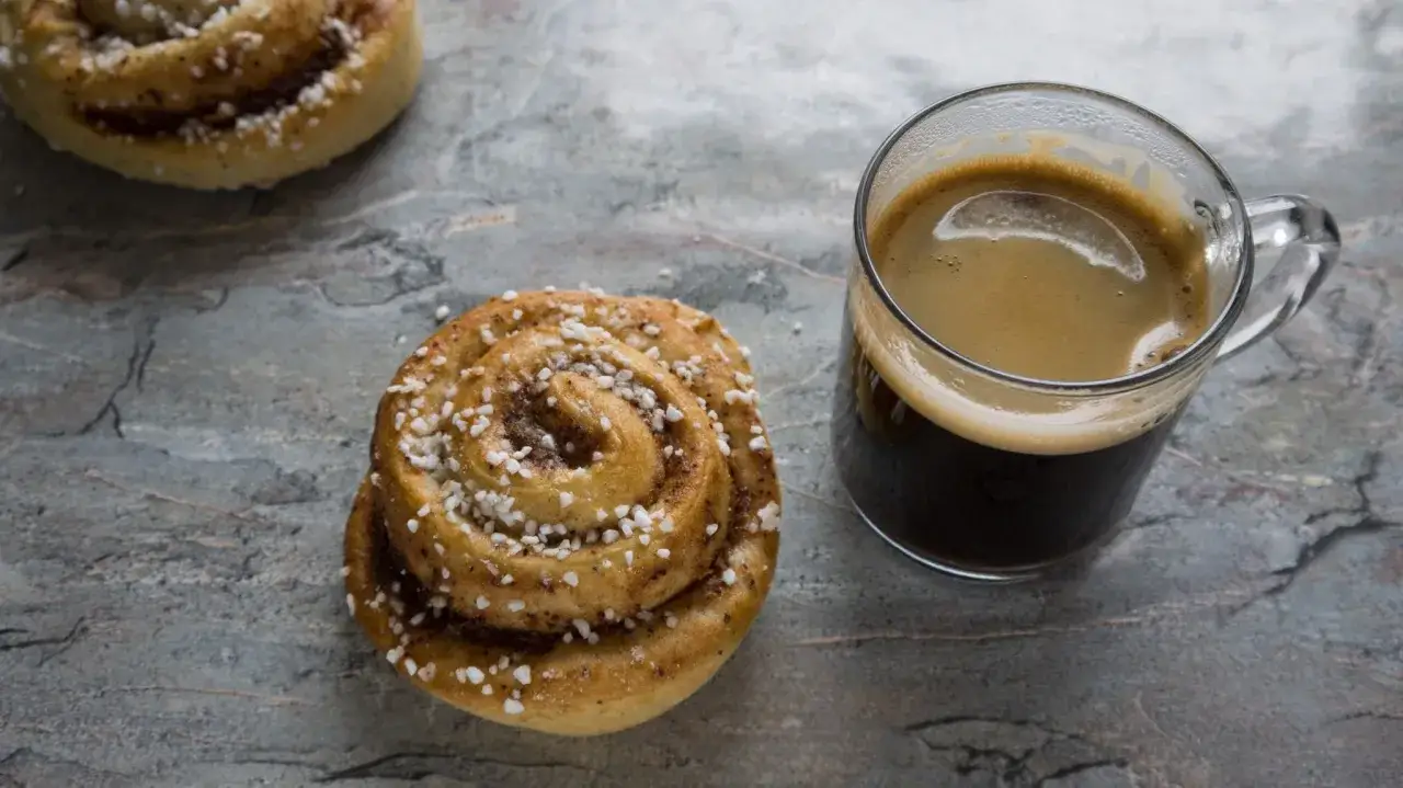 En kanelbulle och en kopp cafe kaffe på en stenig yta.