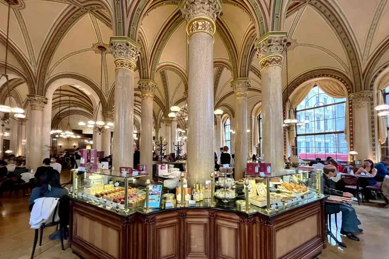 Ett elegant kafé med välvda tak och pelare. I förgrunden syns ett dessertbord med bakverk, perfekt för en wiener melange kaffe.