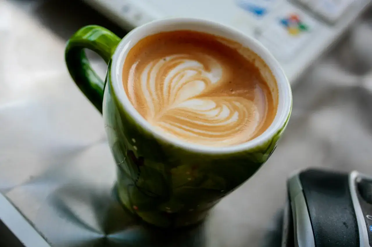 En grön mugg med en vacker kaffe macchiato med hjärtmönster i skummet.