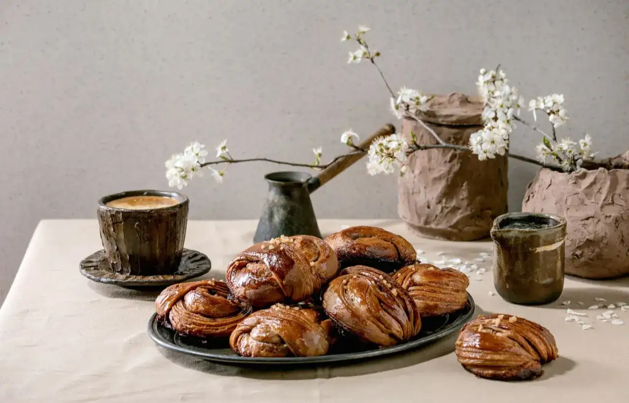 En kopp kaffe och en tallrik kanelbullar, perfekt för ett mysigt kaffe test. Blommor i bakgrunden ger en vårkänsla.