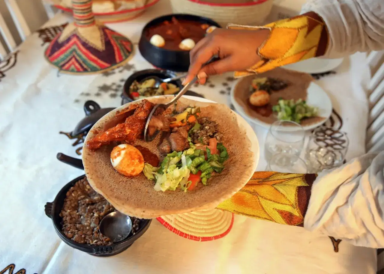 En hand tar en bit från en tallrik med eritreansk kaffe, injera och olika grytor.