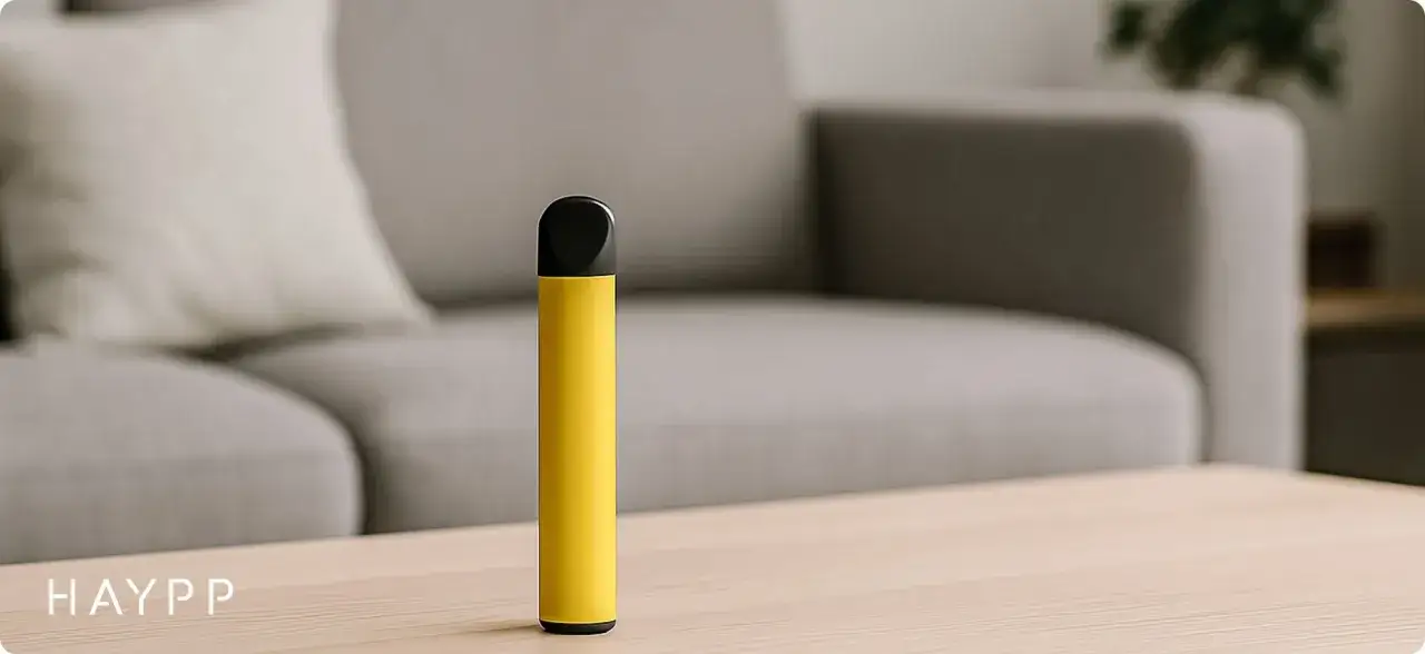 En gul vape ligger på ett bord framför en soffa. En diskret vape inomhus för en avslappnad stund.