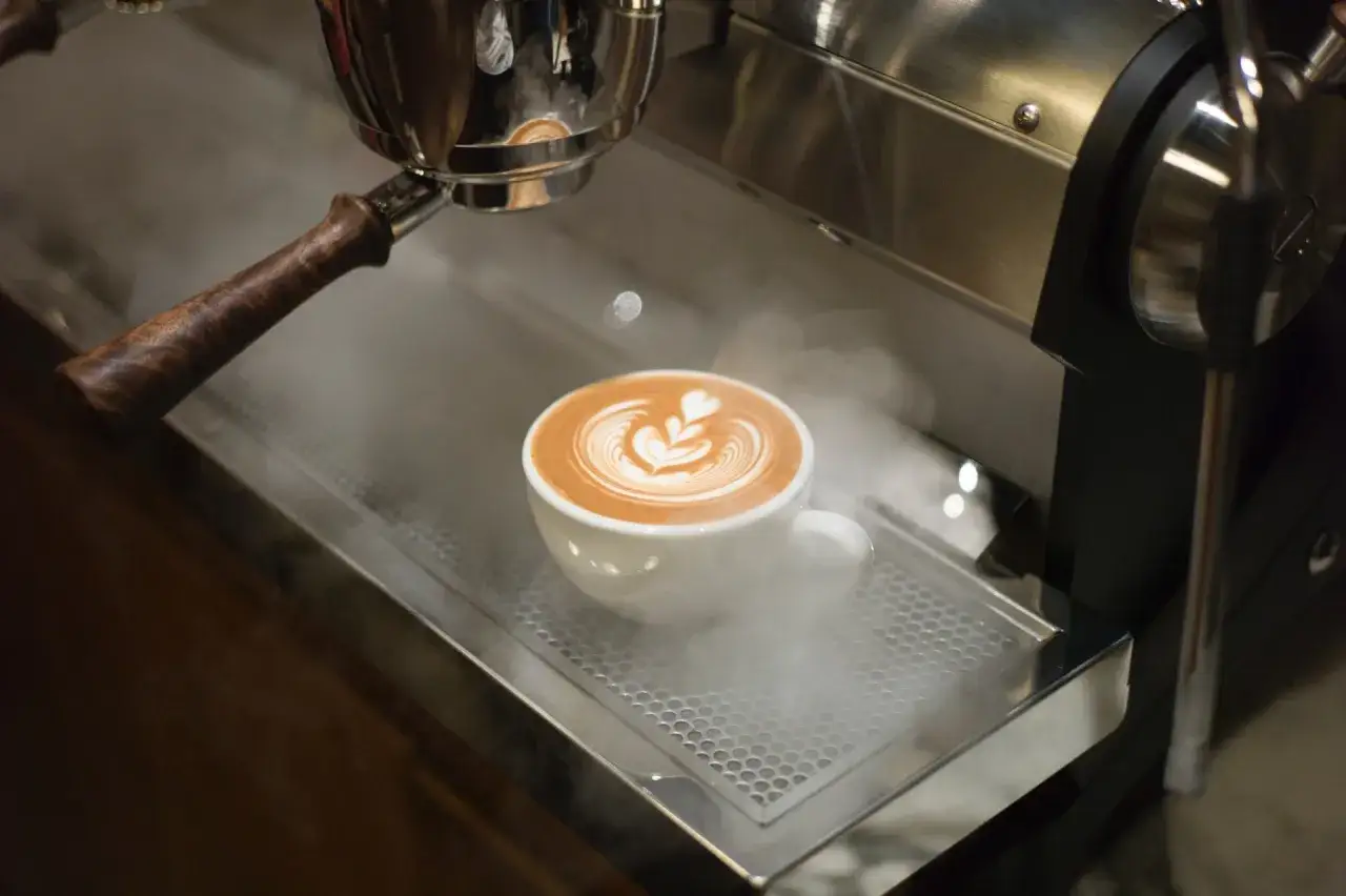 En vit kopp med latte art, omgiven av ånga. Den lena kaffeskummet har ett vackert mönster.