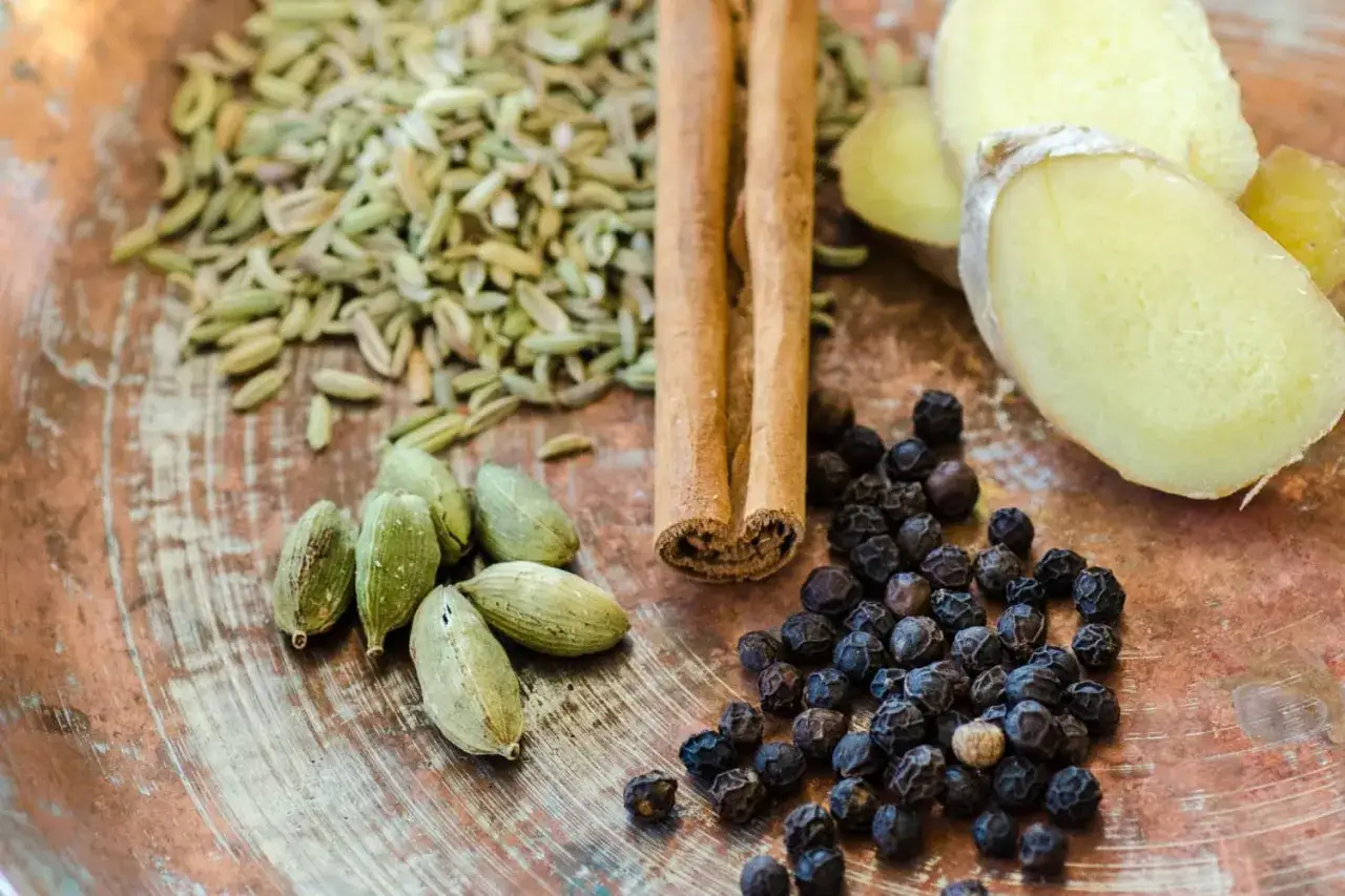 Kardemumma, kanel, fänkålsfrön, pepparkorn och ingefära på en koppartallrik. Ingredienserna som ger te smak.