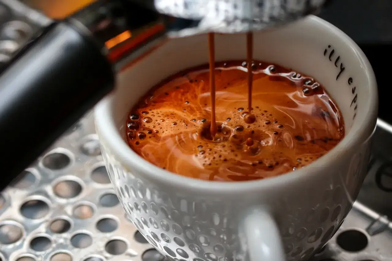 En espresso rinner ner i en vit kopp, redo att bli en cafe americano.