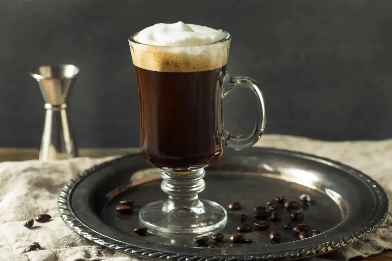En värmande kaffedrink med alkohol, toppad med grädde, på ett fat med kaffebönor.