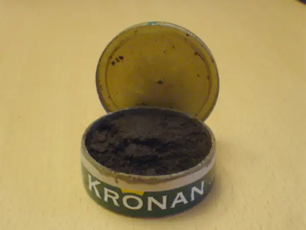 En öppen snusdosa med snus. Kronan-loggan syns tydligt. En klassisk snusdosa storlek.