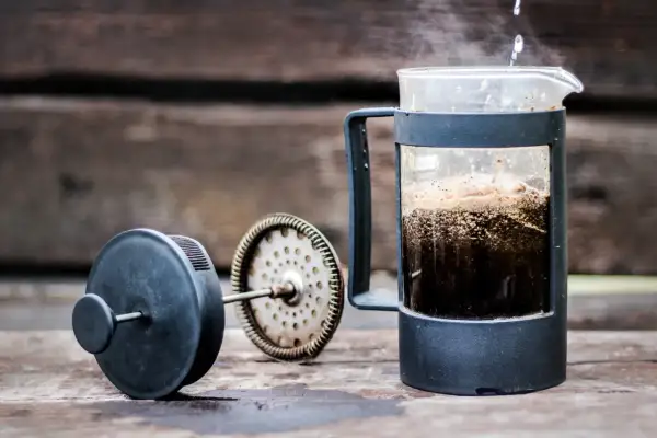 Varmt vatten hälls över kaffepulver i en presskaffe i kaffebryggare. Ånga stiger från den nybryggda drycken.